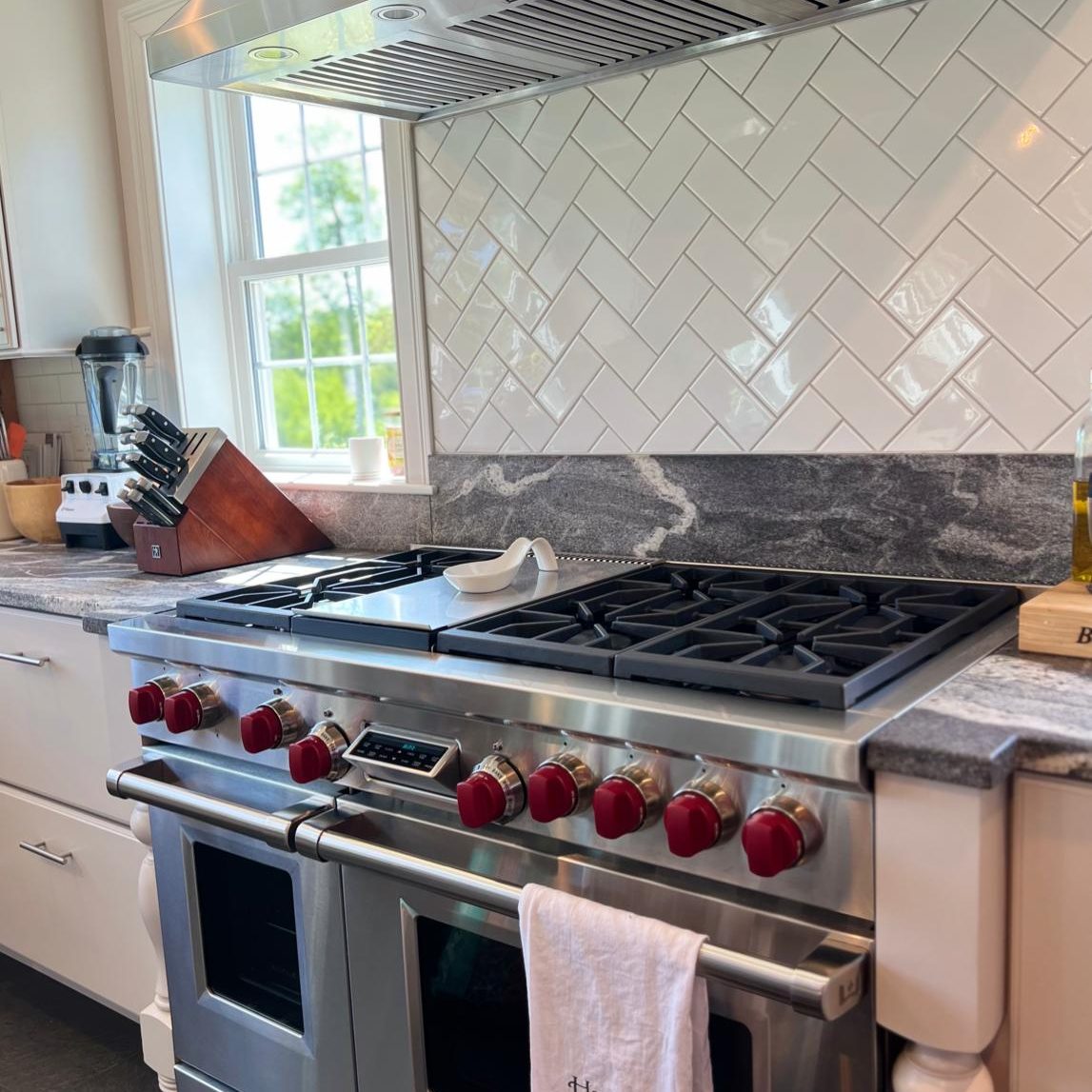 Deep-cleaned high-end stainless steel gas range and vent hood with a sparkling white herringbone tile backsplash in a move-in ready kitchen.