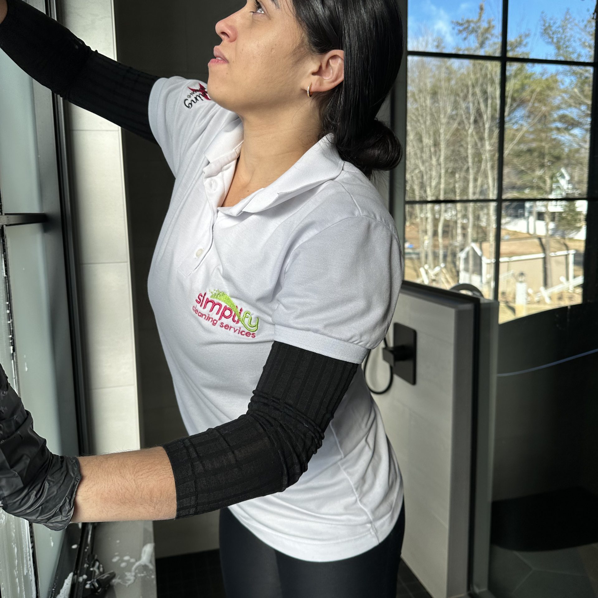 Professional cleaner in uniform and protective gloves sanitizing a stainless steel dishwasher handle during a deep kitchen clean.