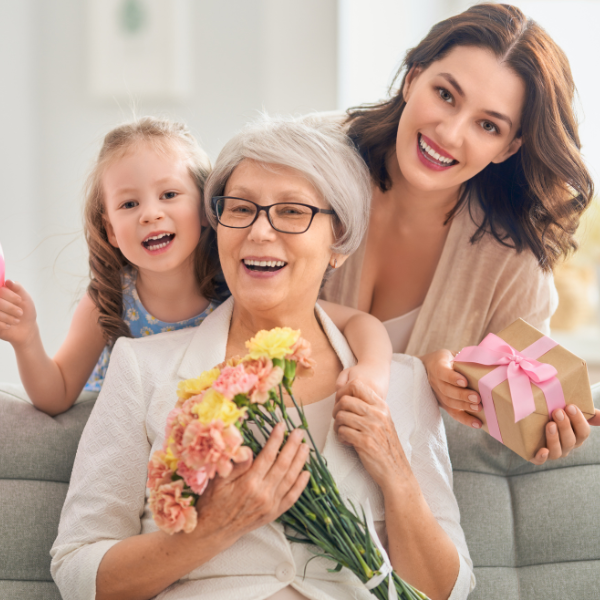 A woman and her young daughter present a grandmother with flowers and a gift card for maid services.